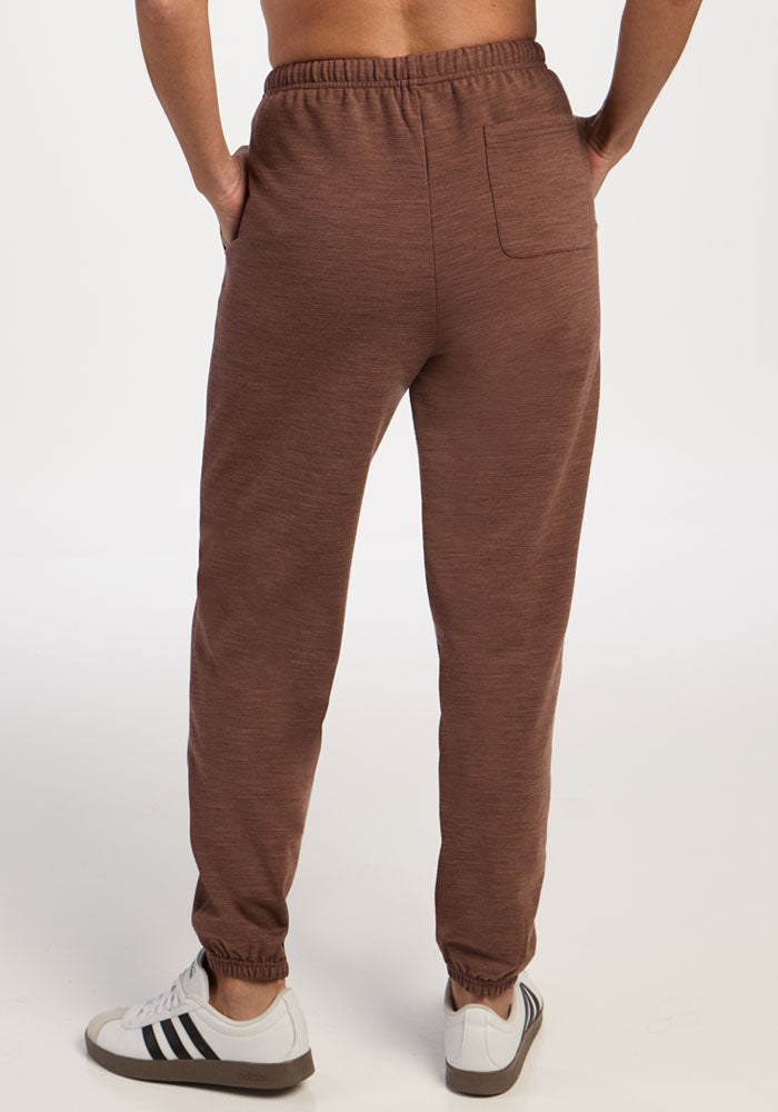Person in Woolx Juliette Joggers - Sable Heather, moisture-wicking, hands in pockets, back view with white sneakers.