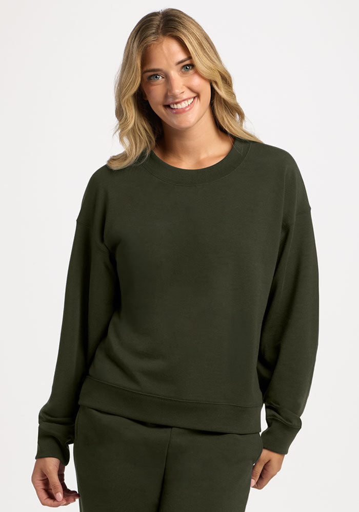 A smiling woman wearing a dark olive green Molly Crewneck - Duffel Bag merino wool sweatshirt. 