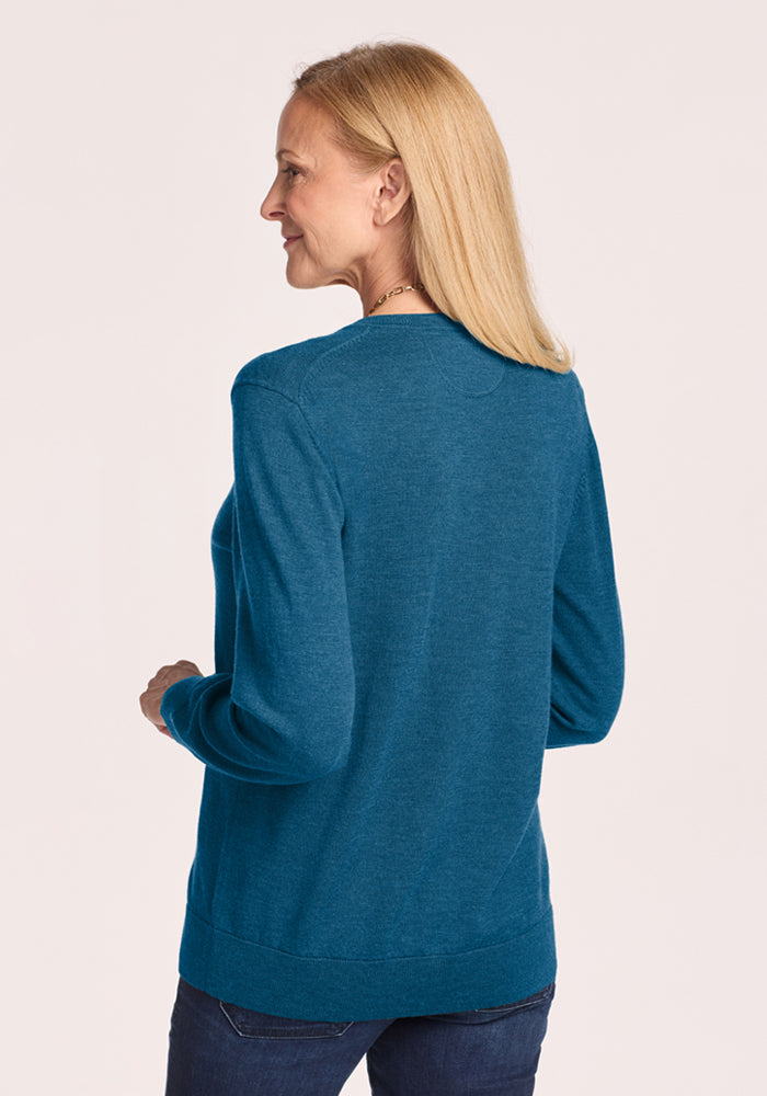 Woman with blonde hair in Woolx Francesca Sweater - Blue Pine and jeans stands facing away against a light background.
