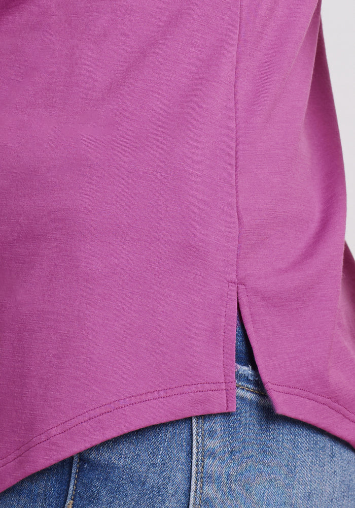 Close-up of a person wearing the Woolx Bella Tunic Top in Purple Wine, paired with light blue denim jeans. The lightweight merino texture and detailed stitching of the tunic are clearly visible.