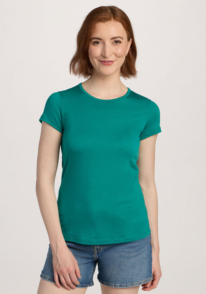 A woman smiles against a plain background wearing the Woolx Addie Crew Neck - Cabana Crush and denim shorts. 