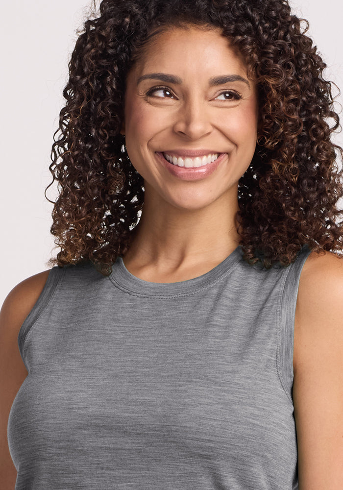 A woman with curly brown hair smiles while looking off to the side, wearing the Woolx Bella Tunic Top in Graphite Heather against a light background.
