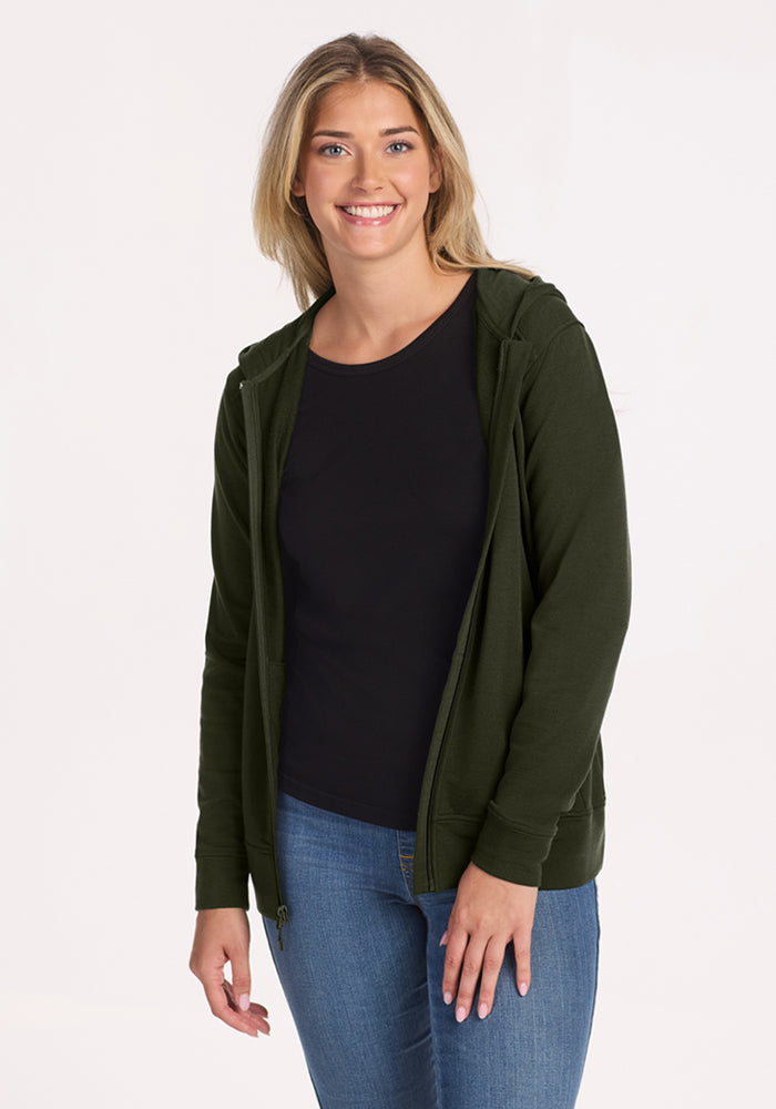 A woman in the Woolx Darby Zip Up Hoodie - Duffel Bag smiles in a black shirt and jeans against a light background.