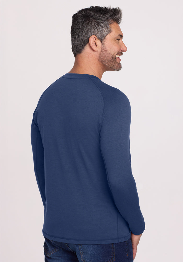 A man with short dark hair and a beard smiles to the side, wearing the Woolx Essential Tee - Starry Night with dark jeans. The background is plain and light-colored.