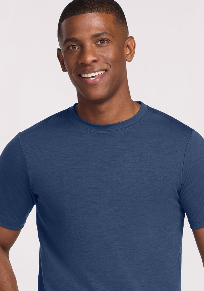 A smiling man with short hair is wearing the Woolx Endurance Tee in Starry Night, standing against a light, neutral background.