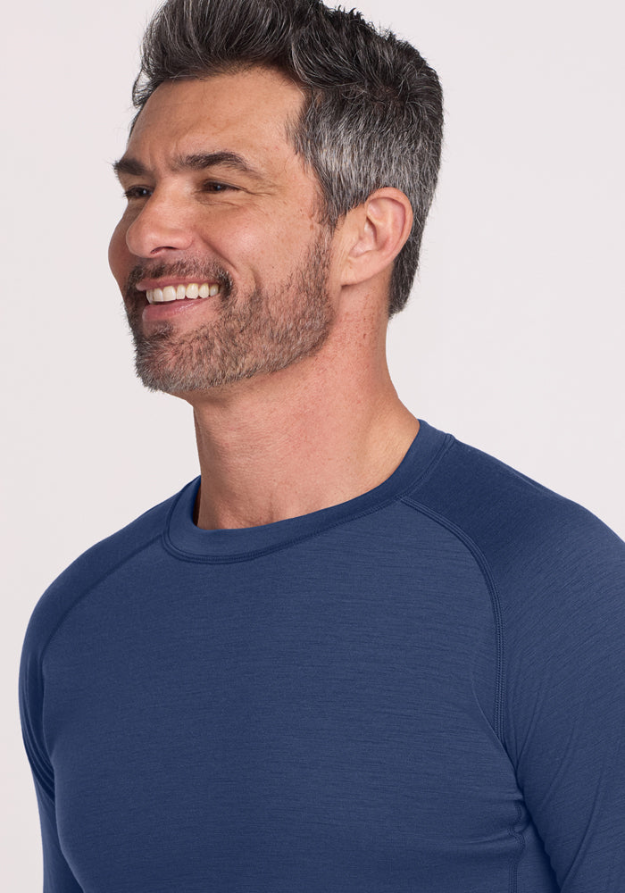 A smiling man with short, dark hair and gray streaks, a trimmed beard, wearing the Woolx Essential Tee - Starry Night, shown from the chest up against a light background—ideal for temperature regulating comfort.