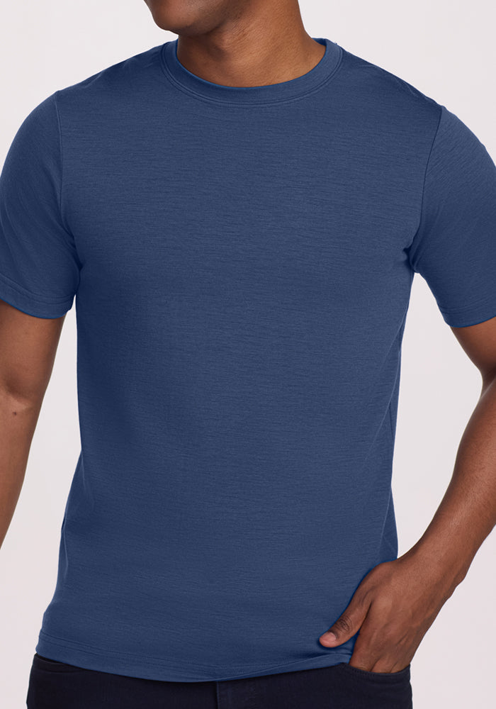 A person wears the Woolx Endurance Tee in Starry Night, a short-sleeved blue Merino wool shirt. The image is cropped from shoulders to hips with one hand in their pocket against a plain light background.