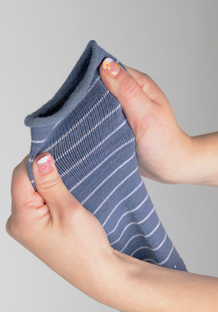 Two hands with colorful flower nail art stretch the Woolx Womens Derby Roll Top Sock in Vintage Indigo with white stripes against a plain light gray background.