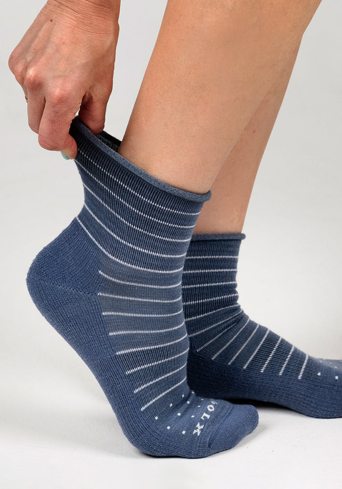 A person pulls up a Woolx Womens Derby Roll Top Sock in Vintage Indigo with white stripes; another matching sock is worn on the other foot. The cushioned sole socks pop against a plain, light-colored background.