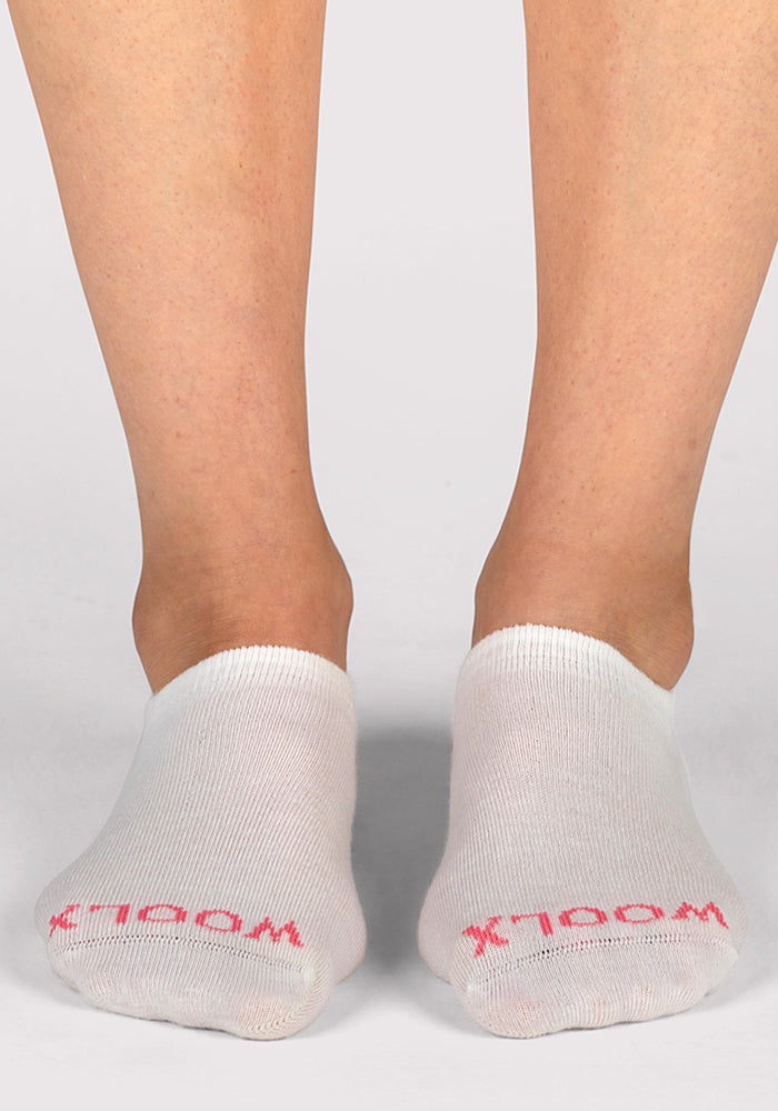 A pair of feet wear Woolx Womens Daisy Ped Socks in Sweet Peony, featuring "WOOL" in pink near the toes, photographed from the front against a plain light background.