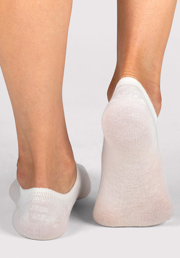 A close-up rear view of two feet wearing Woolx Womens Daisy Ped Socks in Sweet Peony, standing on a light gray surface. The no-show socks fully cover the feet while staying hidden below the ankles for a sleek, minimal look.