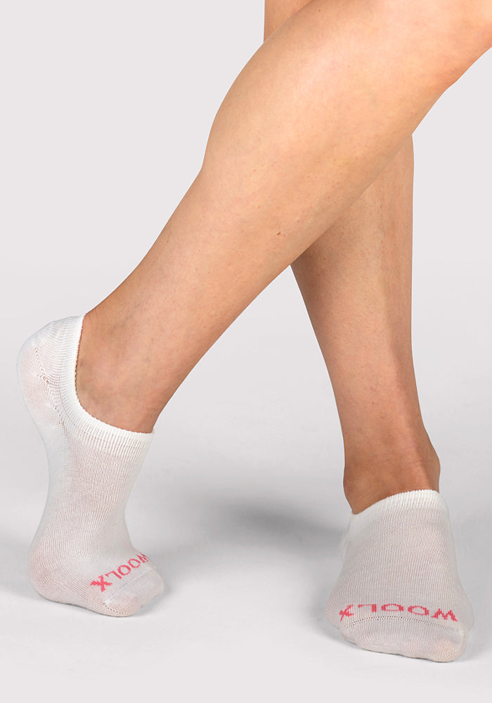 A person models Woolx Womens Daisy Ped Socks in Sweet Peony, crossing one leg over the other against a light background.