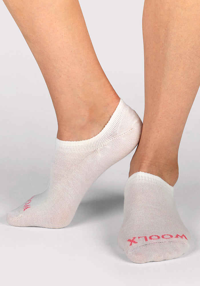 Close-up of a person wearing Woolx Womens Daisy Ped Socks in Sweet Peony, standing on tiptoe with one foot slightly behind the other against a plain light background.