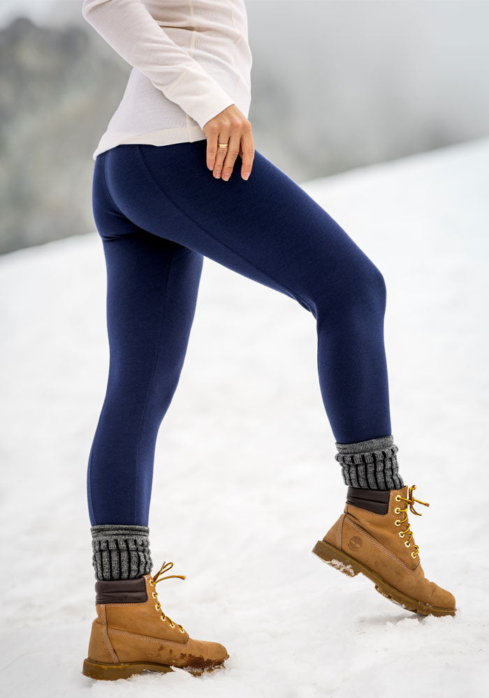 Person in Woolx Stella Petite - Ocean Cavern leggings, tan boots, and gray socks stands on snow with one leg raised.