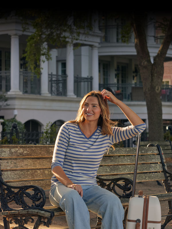 Model wearing blue sand stripe Elena v neck sitting on bench mobile size