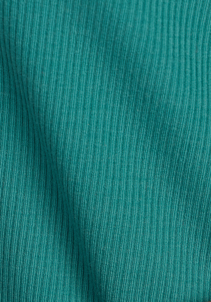 Close-up of the Woolx Delia Ribbed Short Sleeve - Surfside, featuring teal ribbed fabric with a fine vertical texture and gentle diagonal fold, perfect for a relaxed merino wool top.