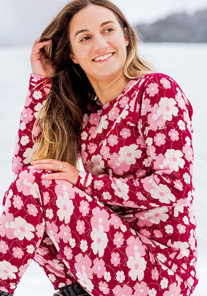 A smiling woman wearing a Maddie Baselayer Top - Floral Crush and matching leggings with a pink and red floral pattern.