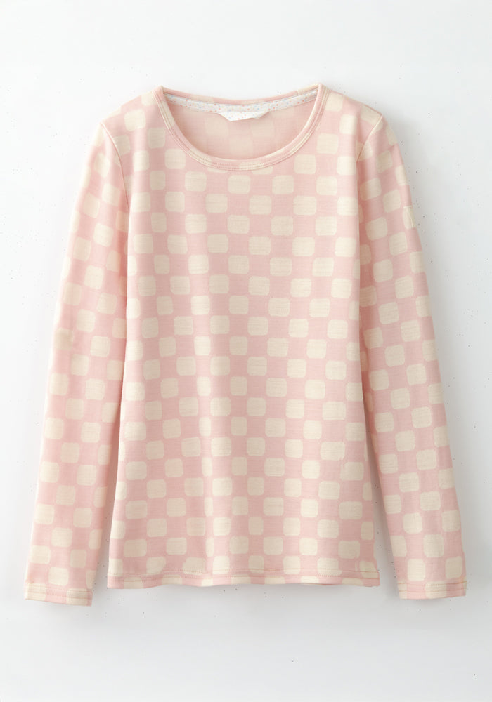 The Woolx Kids Explorer Base Layer Top in Hopscotch Pink features long sleeves, a round neck, and cream square patterns. Made from moisture-wicking Australian Merino wool for all-day comfort. Displayed against a white background.