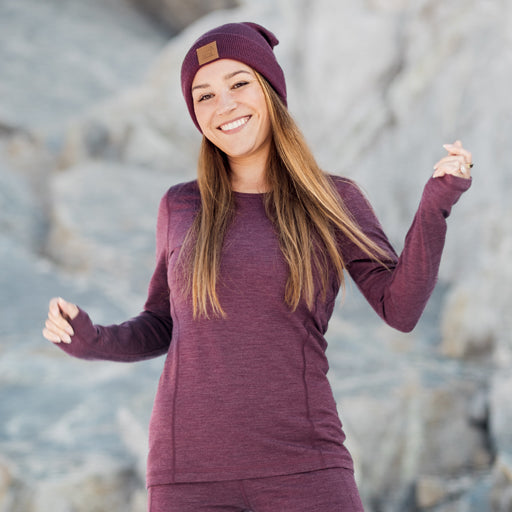 Woman wearing a purple outfit with a beanie standing against a rocky background