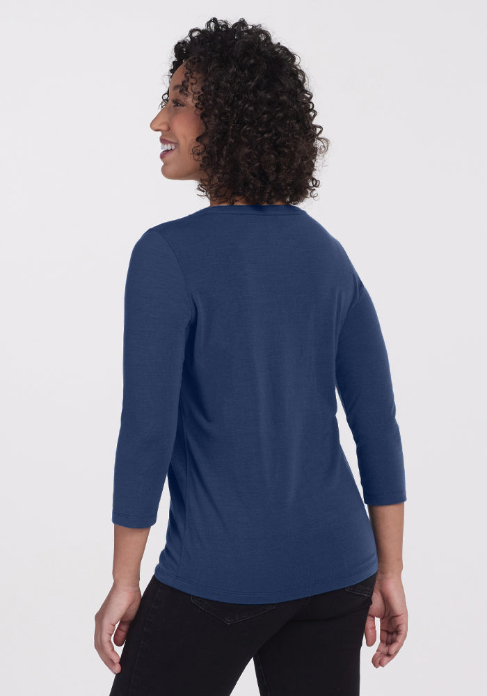 A person with curly hair, wearing the Woolx Jenny 3/4 Sleeve Crew Neck in Starry Night and black pants, stands facing away from the camera, smiling over their shoulder against a plain white background.