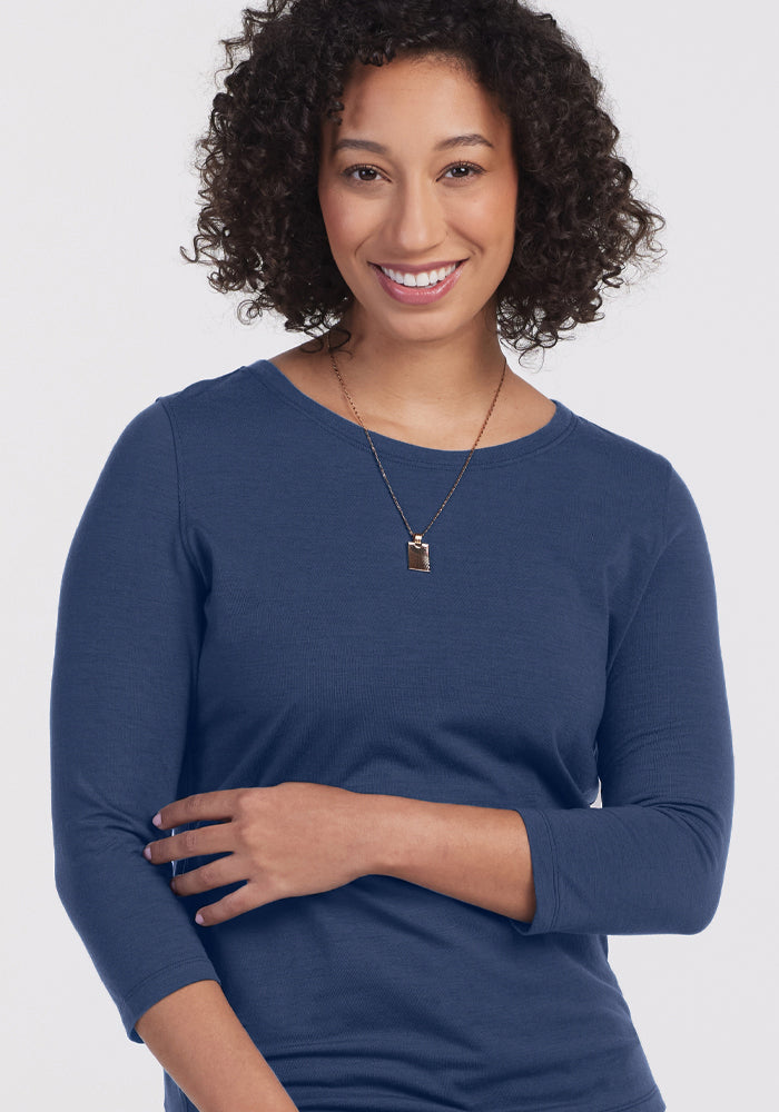 A woman with curly hair, wearing the Woolx Jenny 3/4 Sleeve Crew Neck in Starry Night and a necklace, smiles at the camera against a plain light background.