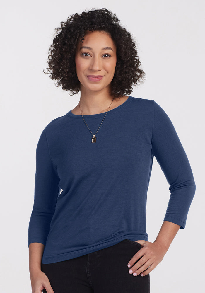 A woman with curly dark hair wears the Woolx Jenny 3/4 Sleeve Crew Neck in Starry Night, along with a necklace, standing against a plain white background and smiling slightly with one hand on her hip.