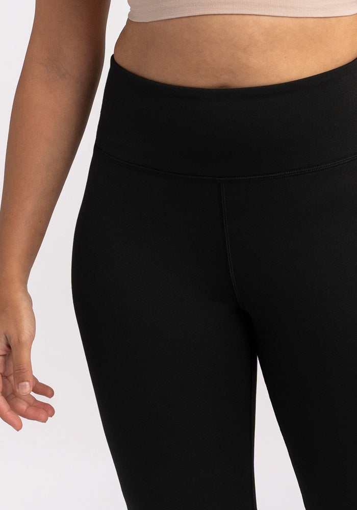 A person in a beige crop top and Woolx Marissa Tall Pants in black stands with one arm relaxed by their side.