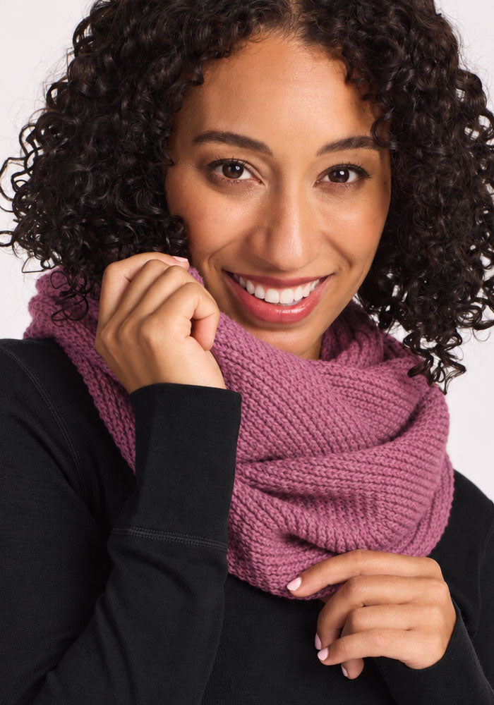 Smiling woman with curly hair wears Woolx Noelle Infinity Scarf - Toasted Rose, cozy and held close to her face.