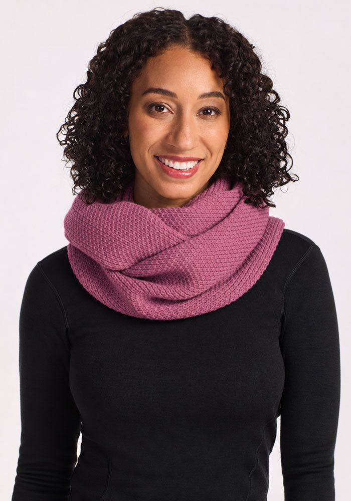 Woman with curly hair smiles, wearing the Woolx Noelle Infinity Scarf in Toasted Rose and a black top.