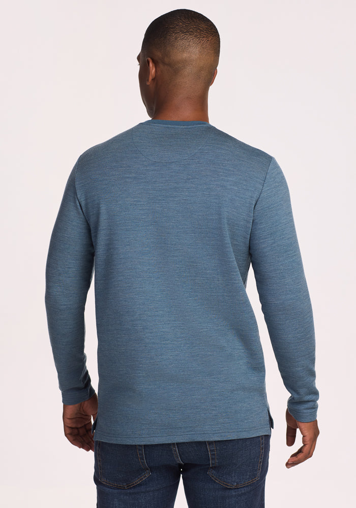 A man faces away from the camera, wearing the Woolx Jackson Henley in Steel Blue and dark blue jeans, set against a simple light background.