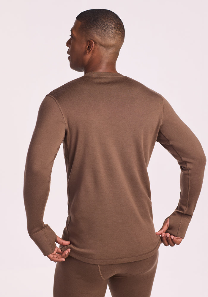 A man is shown from the back, standing with hands on hips, wearing the Woolx Glacier Long Sleeve Crew and matching bottoms in Bourbon Oak against a plain light background.