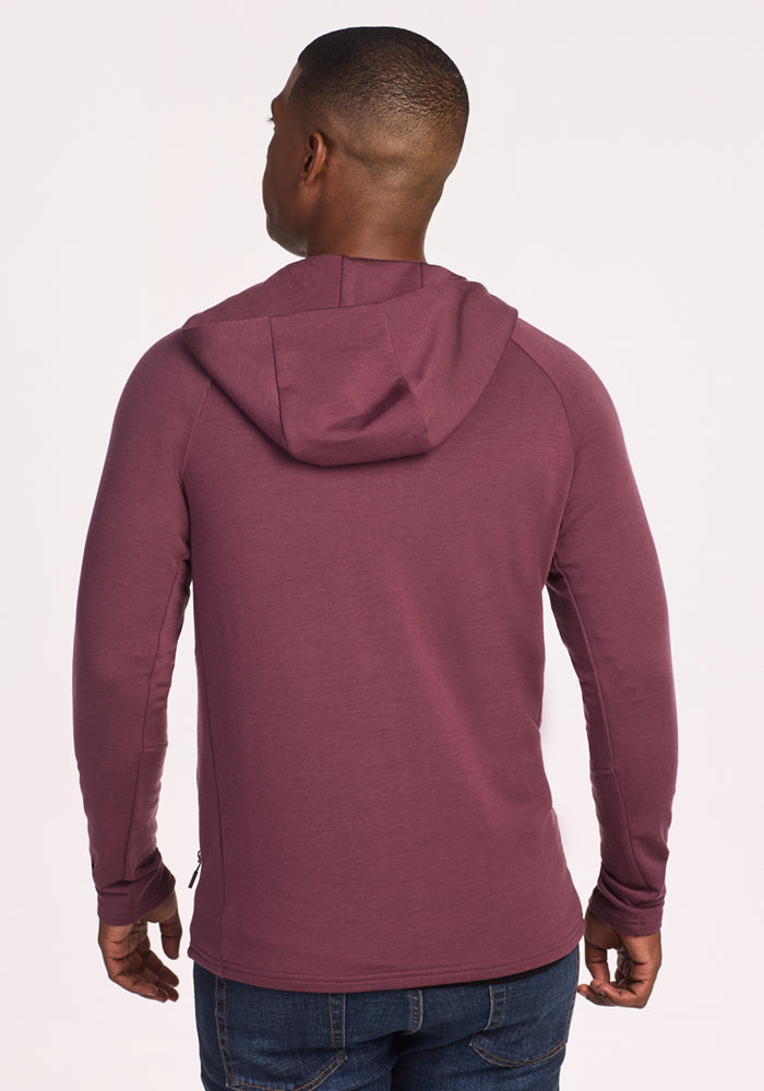 A person wearing the Woolx Boulder Hoodie in Grape Harvest and blue jeans stands facing away from the camera against a plain light background.