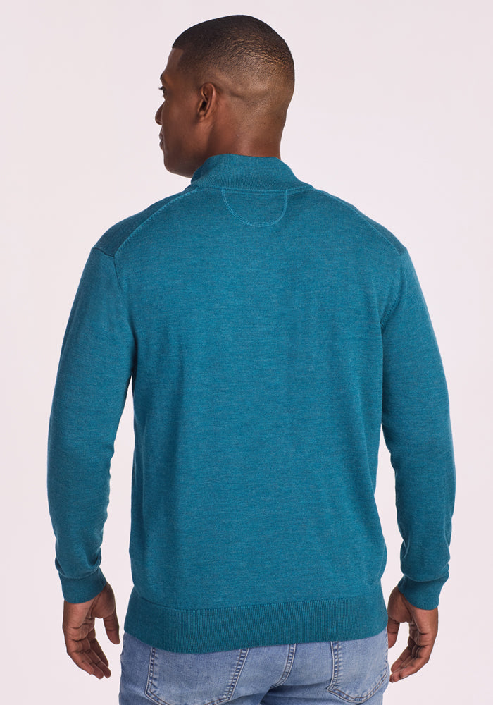 A man faces away from the camera wearing the Woolx Enzo Quarter Zip in Harbor Teal and light blue jeans, set against a plain, light-colored background.
