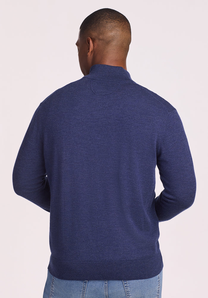 A man faces away from the camera, wearing a Woolx Enzo Quarter Zip in Twilight Storm and light blue jeans against a plain light background.