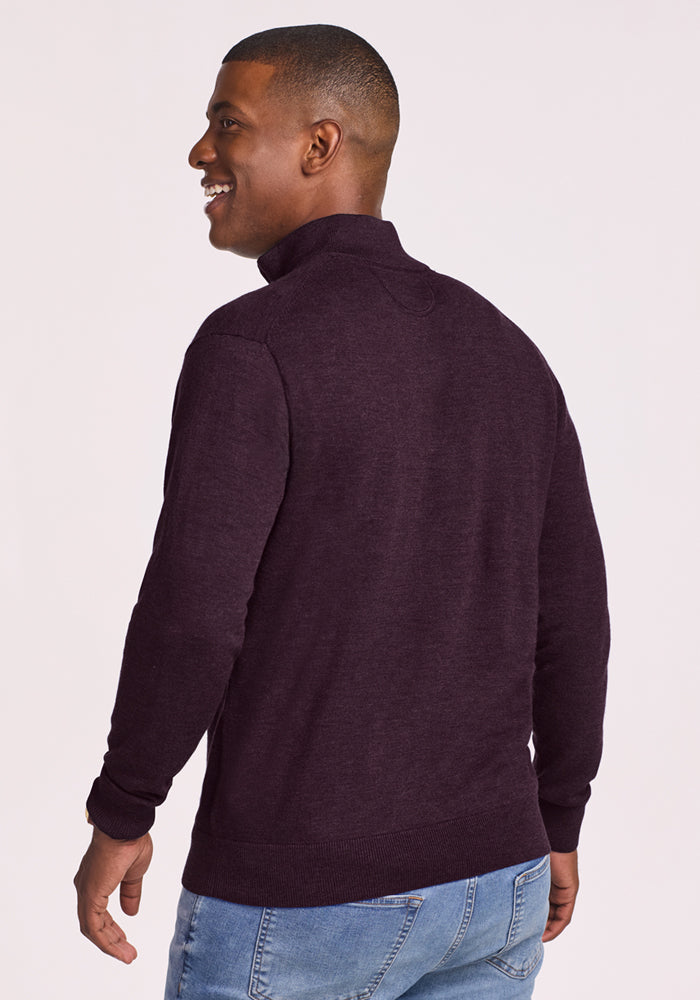A man in the Woolx Enzo Quarter Zip - Deep Plum sweater and blue jeans stands facing away, turning his head to the side and smiling against a light background.