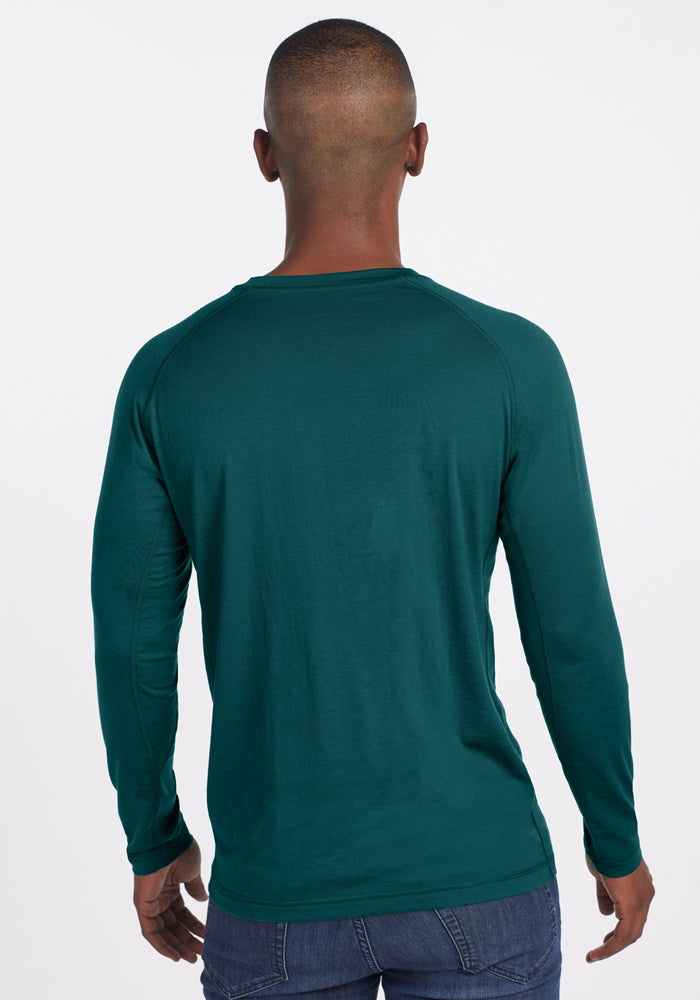 A person with short hair is seen from behind wearing the Woolx Essential Tee in Riverbank Green and blue jeans, set against a plain white background.