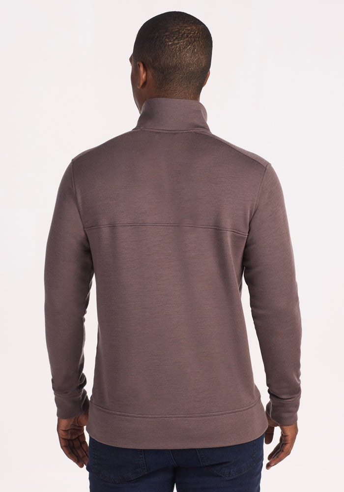 A man stands with his back to the camera, wearing the Woolx Mason 1/4 Zip fleece in Plum Truffle and dark blue jeans, set against a plain light background.