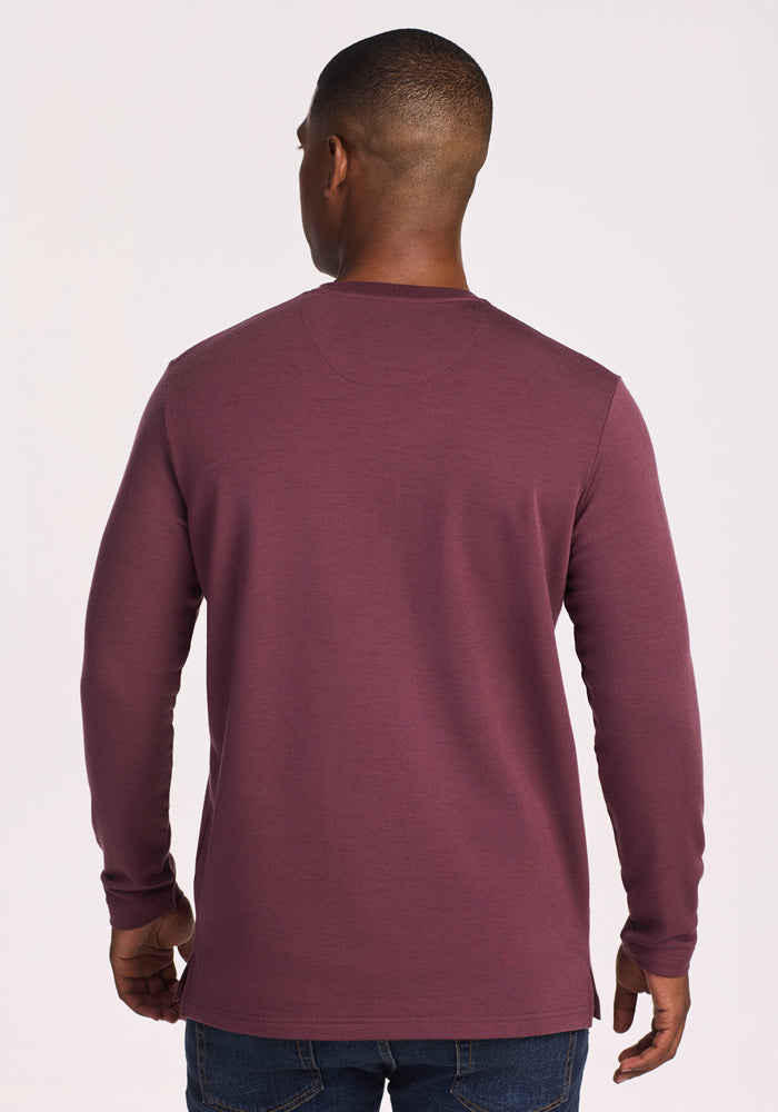 A man faces away from the camera, wearing the Woolx Jackson Henley in Grape Harvest and blue jeans, set against a plain light background.