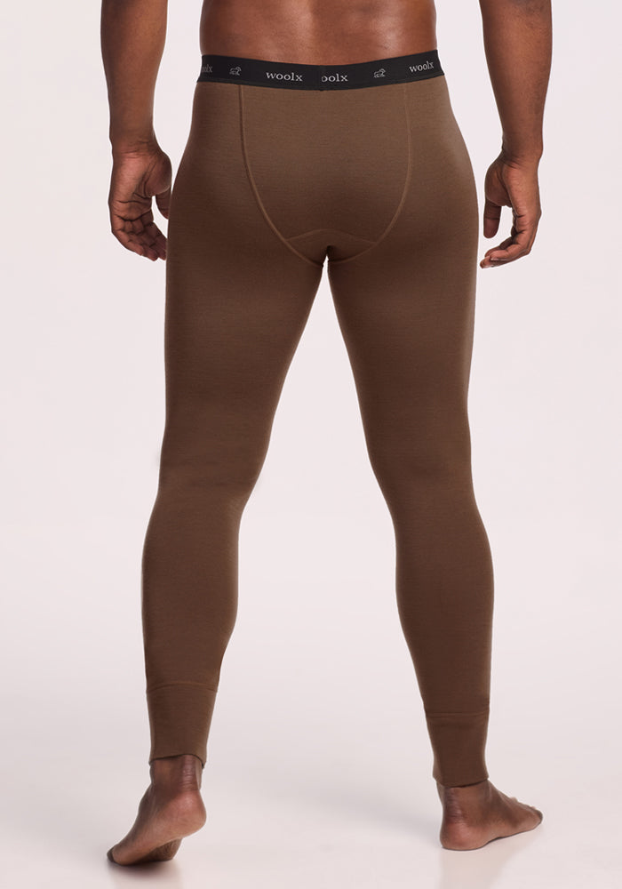 A man stands barefoot facing away, wearing Woolx Backcountry Leggings in Bourbon Oak—a fitted merino wool base layer with a black waistband featuring the "woolx" brand name in white.