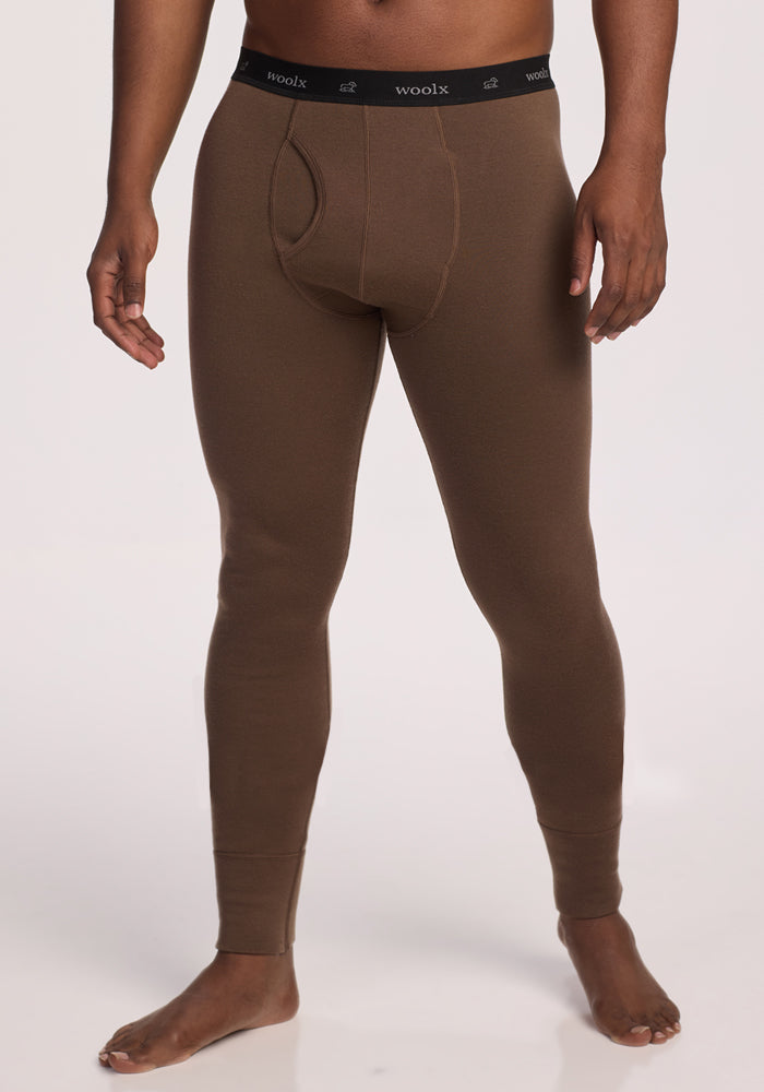 A man stands barefoot wearing Woolx Arctic Leggings in Bourbon Oak, featuring a black waistband printed with "woolx." The ultra-heavyweight Merino wool leggings are shown against a plain white background.