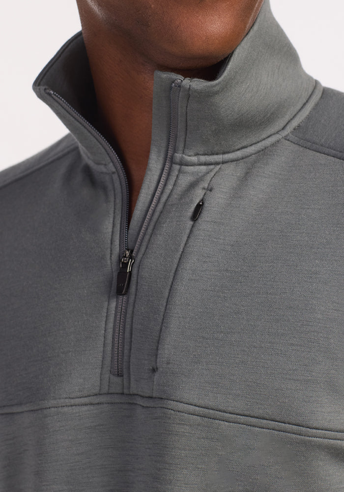 A close-up shows a person in the Woolx Mason 1/4 Zip pullover in Sedona Sage, made from recycled polyester. The collar is partly unzipped, highlighting the smooth, subtly textured fabric, with the person's face mostly out of frame.