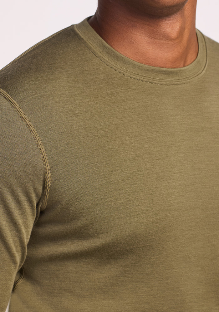A close-up of a person wearing the Woolx Explorer Base Layer in Winter Moss, highlighting the upper chest, neck, and shoulder with visible stitching and textured moisture-wicking fabric.