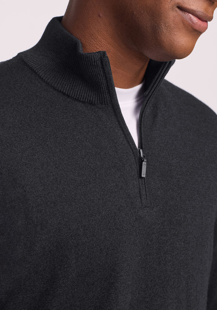 A close-up of a person wearing the Woolx Enzo Quarter Zip - Coal Stone over a white shirt. The partially open zipper reveals the shirt, and the person's face is partly visible with a slight smile.