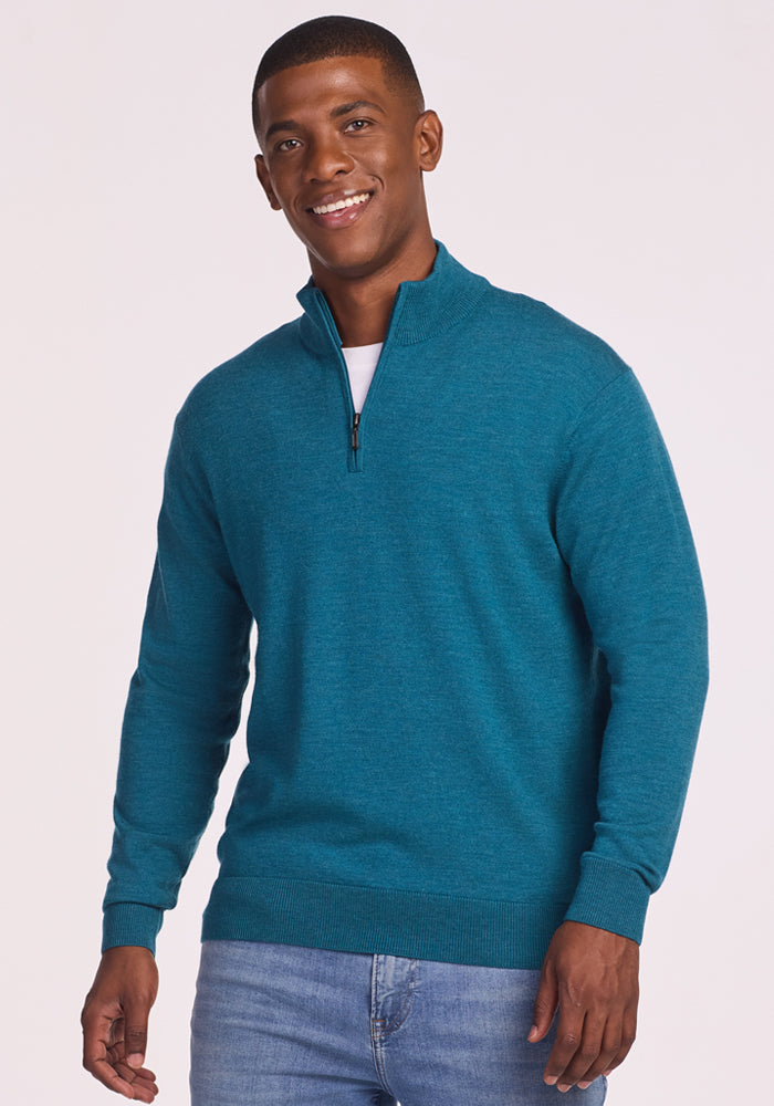Smiling man wearing the Woolx Enzo Quarter Zip in Harbor Teal over a white shirt with light blue jeans, standing against a plain light background. 