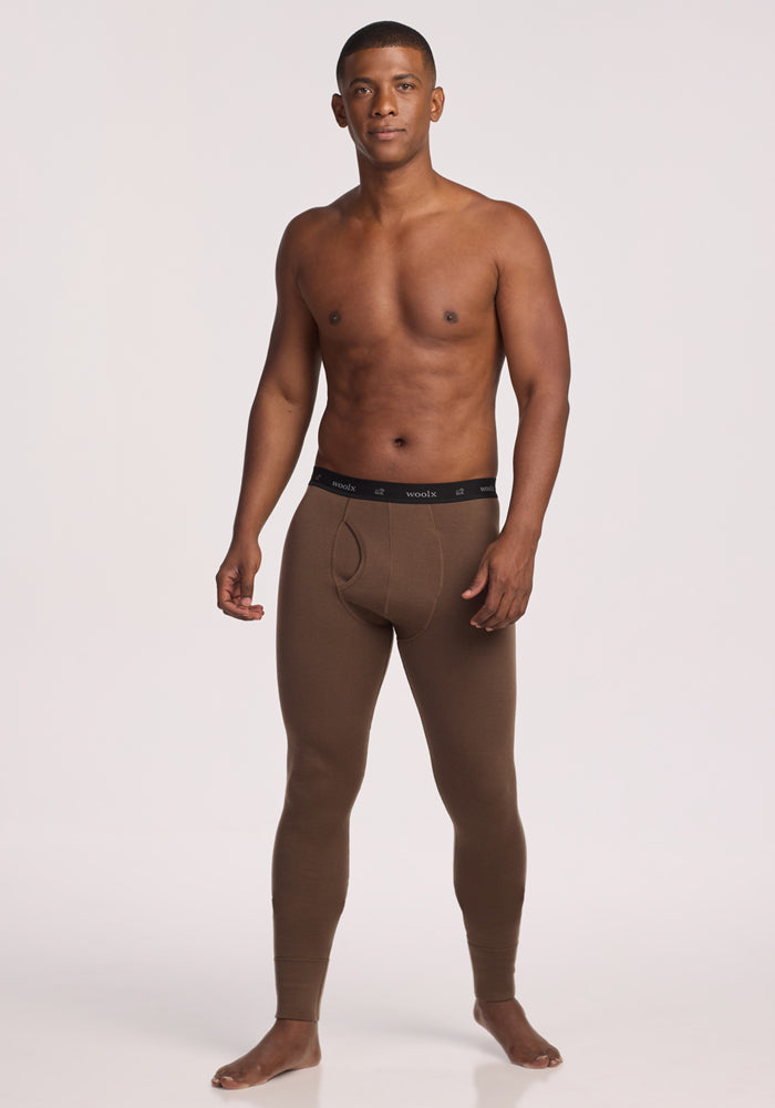 A man stands barefoot against a plain background, wearing Woolx Arctic Leggings - Bourbon Oak and no shirt. He faces forward with a neutral expression.