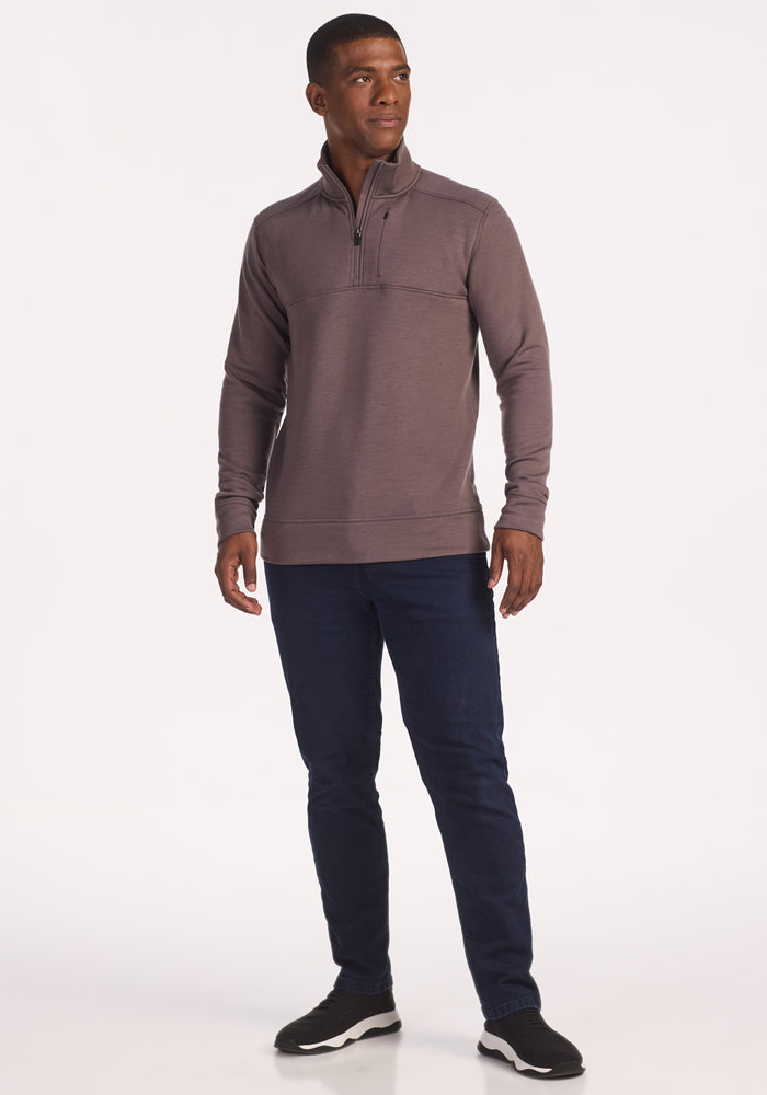 A man stands slightly to the side, wearing the Woolx Mason 1/4 Zip in Plum Truffle, dark blue jeans, and black sneakers against a plain white background.