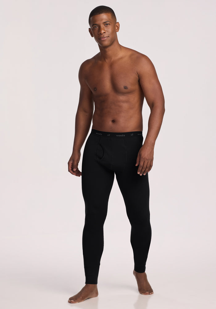 A man stands barefoot against a plain white background, wearing only Woolx Arctic Leggings - Black and no shirt, looking at the camera with a relaxed expression.
