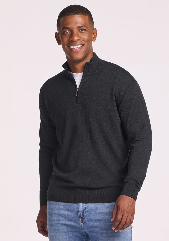A man smiles while wearing the Woolx Enzo Quarter Zip - Coal Stone over a white shirt and light blue jeans, standing against a plain light background. 