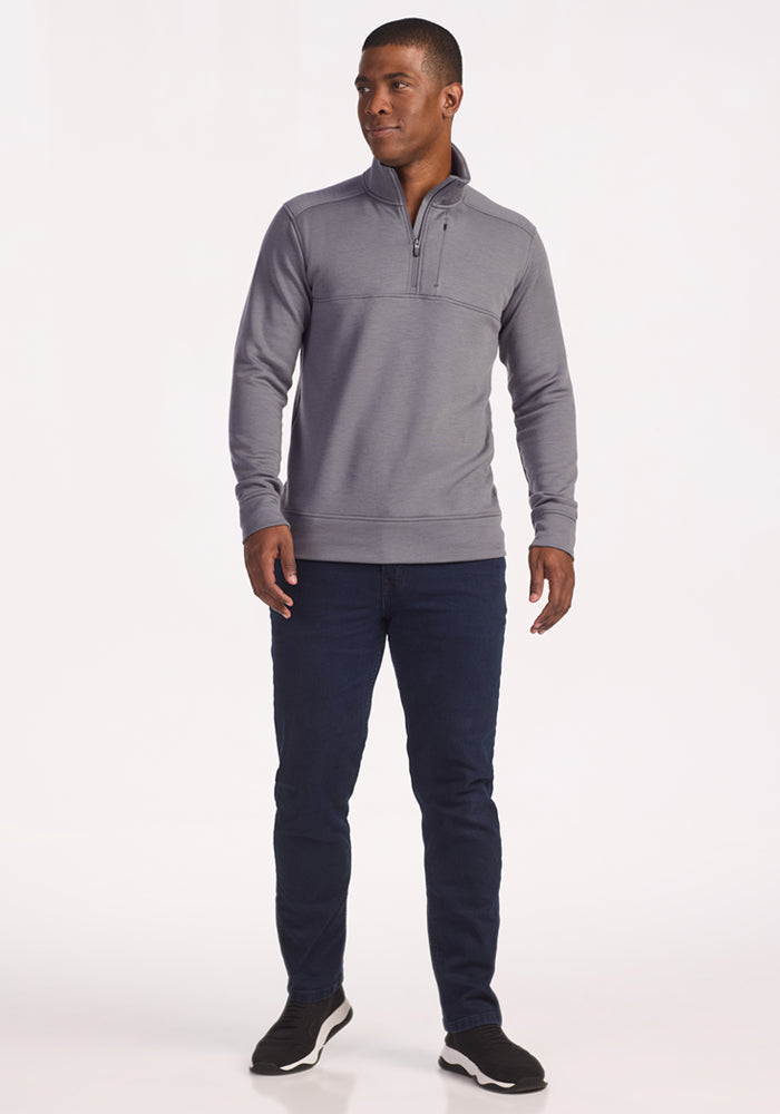 A man stands slightly turned, wearing the Woolx Mason 1/4 Zip in Arctic Dusk, dark blue jeans, and black sneakers against a plain white background.