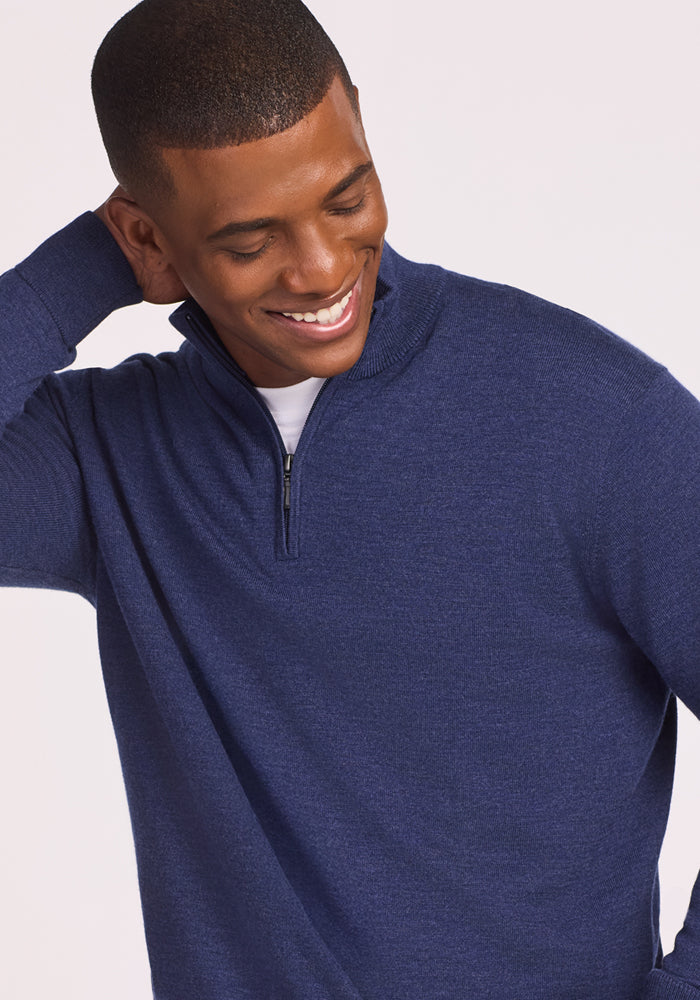 A man in the Woolx Enzo Quarter Zip - Twilight Storm sweater over a white shirt smiles, tilting his head and touching the back of his neck.